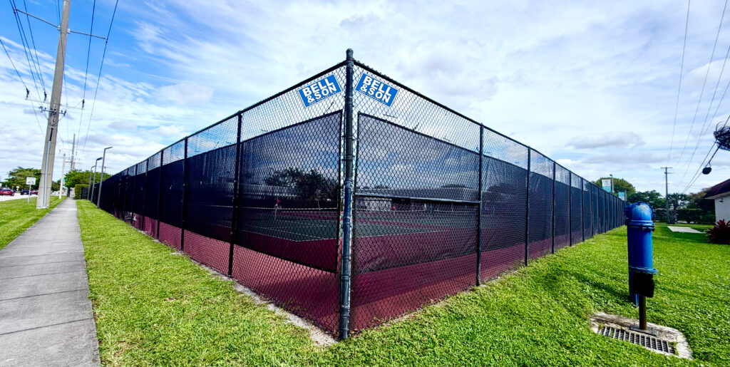 A photo of a finished, green vinyl-coated chain link fence in a recreational setting.